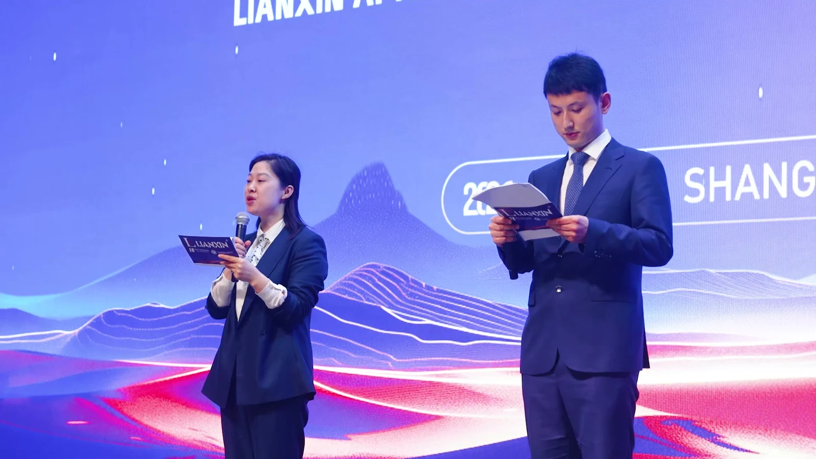 Two presenters holding LIANXIN notes on stage at the evening event