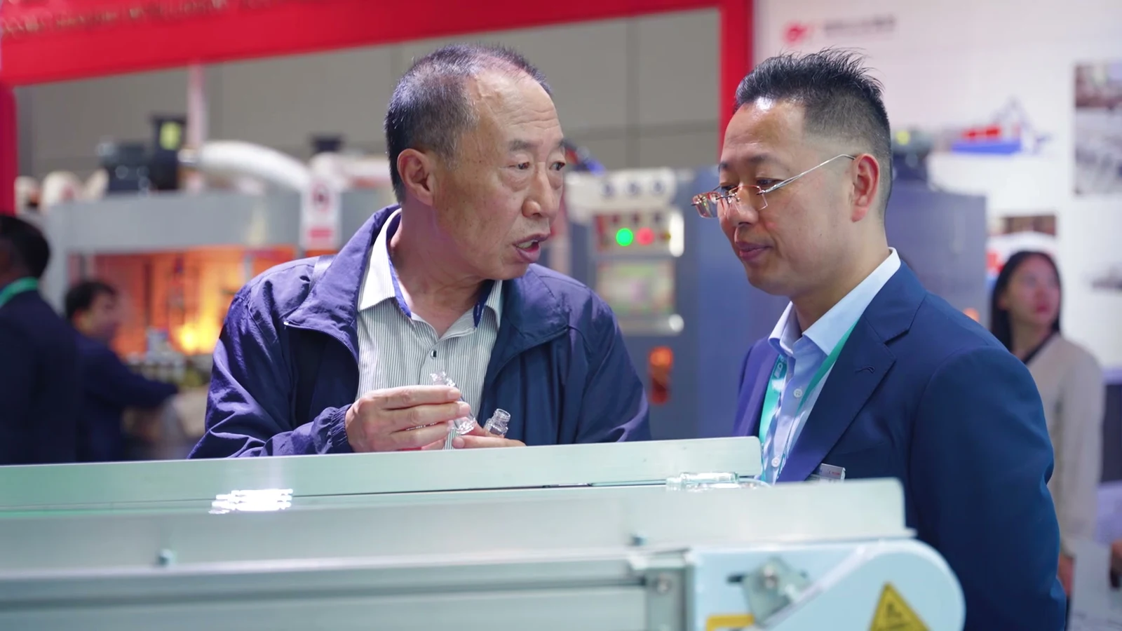 Two people discussing clear bottle samples beside a machine at the exhibition
