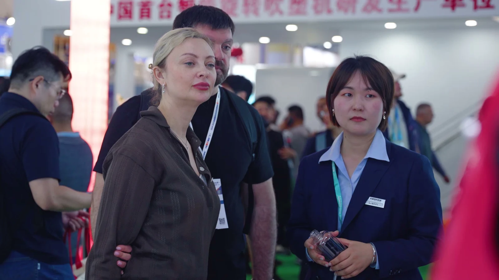 A LIANXIN team member holding a clear bottle sample beside visitors at the exhibition stand