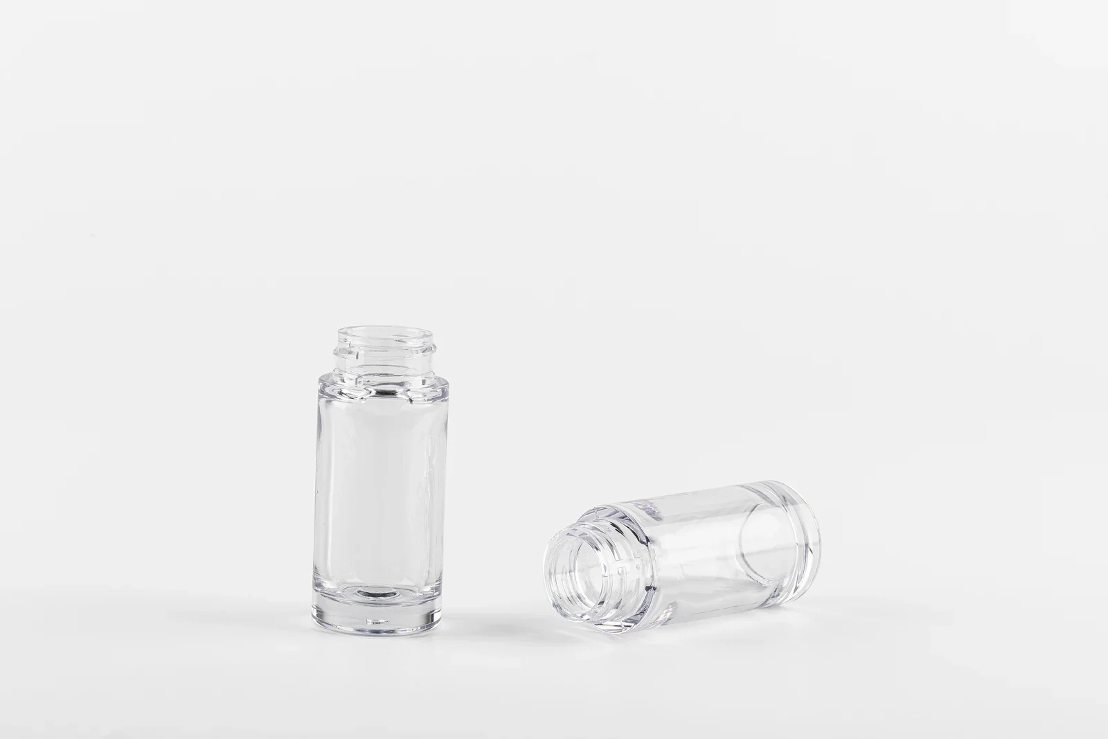Two clear cylindrical cosmetic bottle samples, one upright and one on its side